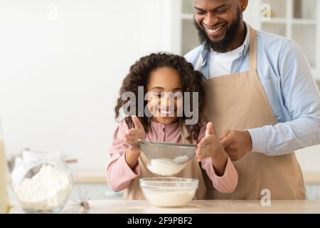 Fröhlicher schwarzer Mann und seine Tochter, die Teig zubereitet Stockfoto