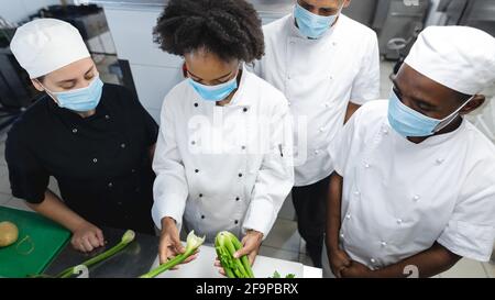 Diverce Rennen männlichen und weiblichen Profiköche Vorbereitung Gemüse mit Gesichtsmasken. Arbeiten in einer geschäftigen Restaurantküche während Coronavirus covid Stockfoto