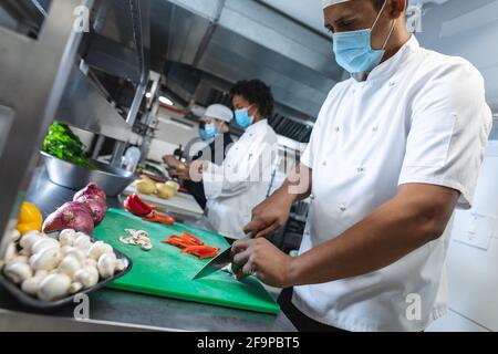 Diverce Rennen männlichen und weiblichen Profiköche Vorbereitung Gemüse mit Gesichtsmasken. Arbeiten in einer geschäftigen Restaurantküche während Coronavirus covid Stockfoto