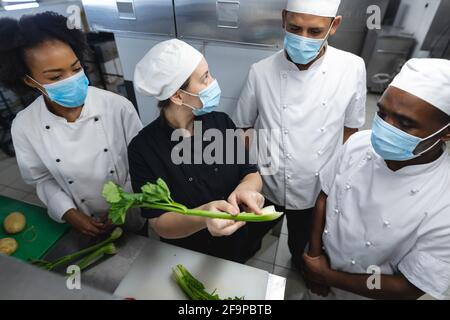 Diverce Rennen männlichen und weiblichen Profiköche Vorbereitung Gemüse mit Gesichtsmasken. Arbeiten in einer geschäftigen Restaurantküche während Coronavirus covid Stockfoto