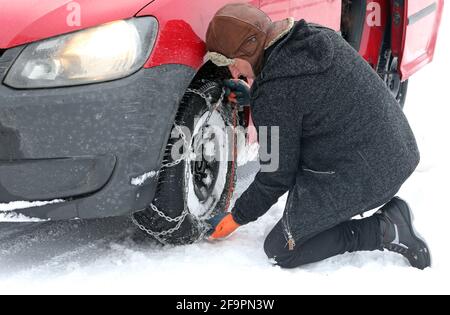 12.02.2021, Graditz, Sachsen, Deutschland - im Winter legt der Mann eine Schneekette auf einen Vorderreifen seines Autos. 00S210212D579CAROEX.JPG [MODEL RELEASE: NO, PROPERT Stockfoto