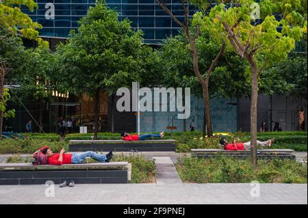 26.10.2018, Singapore, , Singapur - EINE Gruppe südasiatischer Wanderarbeiter ruht nach der Arbeit auf Bänken im Geschäfts- und Finanzviertel von Marina Bay Stockfoto