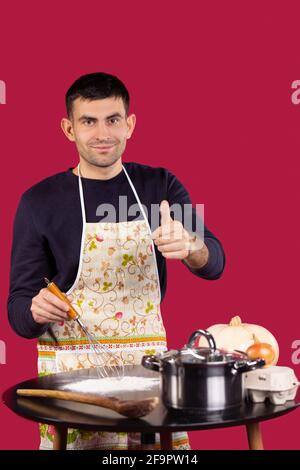 Nahaufnahme des männlichen Küchenchefs, der beim Zubereiten von frisch gemischtem Rezept und beim Kochen Daumen nach oben zeigt. Glücklicher junger Mann, der über dem Gericht steht Stockfoto