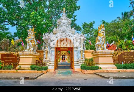 Die szenischen Skulpturen der Singha-Löwen und das verzierte weiße Tor des Wat Phra Singh Tempels, geschmückt mit Naga-Schlangen und Reliefmustern, Chiang Ra Stockfoto