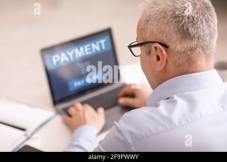 Älterer Mann, der im Büro sitzt, online einkauft und einen Laptop benutzt Stockfoto