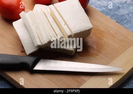 Frisch geschnittener Paneer oder Quark mit Tomaten und Messer auf Schneidebrett. Stockfoto