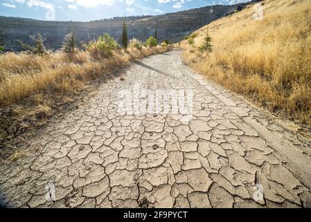 Zugluft in der heißen Sommersaison. Schmutzige Straße in einer bergigen Gegend mit rissigem Lehm und getrockneten Hundepfoten und gelbem Gras auf beiden Seiten der Straße Stockfoto