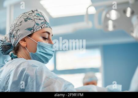 Ein Team von Chirurgen bereitet sich auf die Operation vor. Chirurgen tragen sterile Kleidung vor der Operation mit Hilfe von Krankenschwestern, sterile Kleider, Handschuhe, Masken, in t Stockfoto