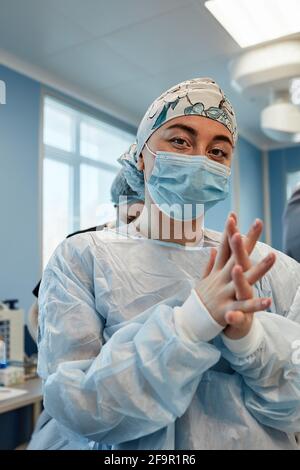Ein Team von Chirurgen bereitet sich auf die Operation vor. Chirurgen tragen sterile Kleidung vor der Operation mit Hilfe von Krankenschwestern, sterile Kleider, Handschuhe, Masken, in t Stockfoto