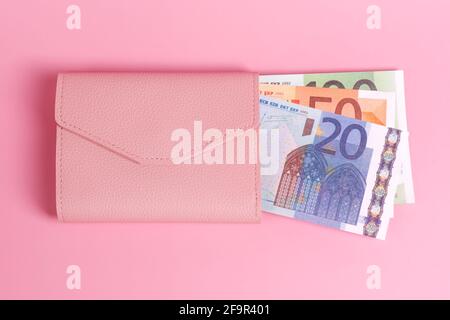 Rosa Geldbörse auf pastellrosa Hintergrund mit Euro-Scheinen darin. Nahaufnahme der modernen Ledergeldbörse und europäischen Banknoten. Finanzen, Investitionen, Sparen, Bargeld Stockfoto