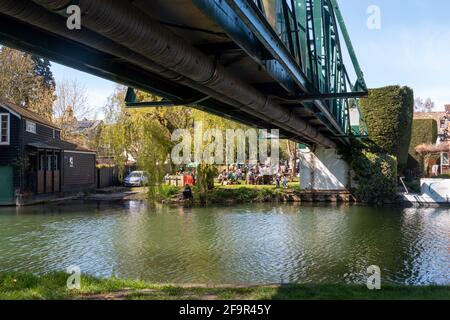 Ein Blick von Stourbridge Common über den Fluss, unter der Brücke, auf den belebten Garten im Green Dragon Pub an einem sonnigen Tag. Cambridge, Großbritannien Stockfoto