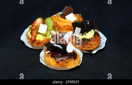 Kunafa mit Früchten und Pistazien auf schwarzem Hintergrund. Ramadan-Süßigkeiten Stockfoto