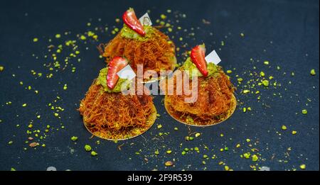 Kunafa mit Früchten und Pistazien auf schwarzem Hintergrund. Ramadan-Süßigkeiten Stockfoto