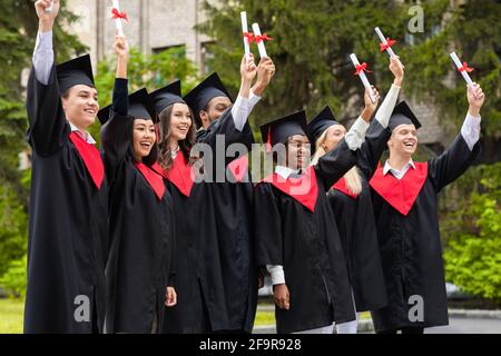 Emotionale multiethnische Studenten in Abschlusskostümen, die Diplome sammeln Stockfoto