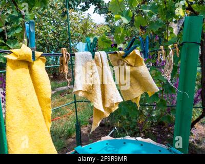 Gelbe nasse Putzlappen trocknen, während sie an einem Draht hängen, der mit Kleidernadeln im Freien auf dem Hof befestigt ist. Ländlicher Hintergrund, einfaches Leben zu Hause Konzept. Stockfoto