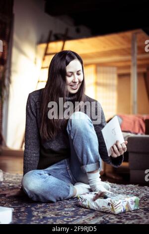 Junge Frau lächelt bei Karte für weihnachtsfeier in gemütlichem Haus Stockfoto
