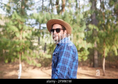 Junger Mann mit Bart und Hut, der die Kamera anschaut Der Wald Stockfoto