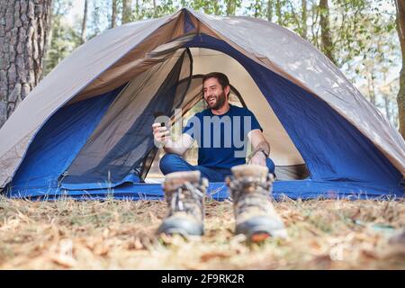 Lächelnder junger hispanischer Mann, der sein Handy in seinem Handy benutzt Zelt Stockfoto