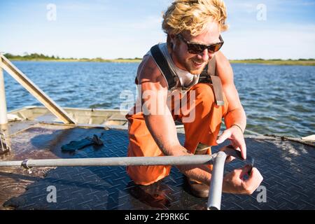 Junger Mann, der am Wasser in der Austernzucht der Aquakultur arbeitet Wartung Stockfoto