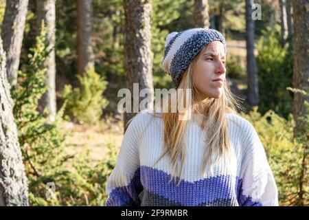 Porträt von jungen schönen kaukasischen Frau in stilvollen Schneehut und Pullover bei Sonnenuntergang.Mode weiblich in Waldlandschaft mit Copy Space. Stockfoto