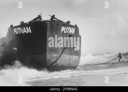 Von der Brandung zerschlagen ein gestrandtes Schiff läuft in der Nähe von Palm Beach, Florida, auf Grund. In der Nähe befindet sich ein Strandkörner, der an einem Seil festhängt. Ca. 1970. Stockfoto