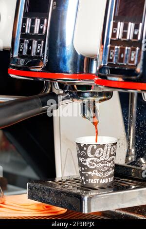 Die Kaffeemaschine gießt aromatischen Kaffee in eine Pappbecher. Vertikales Bild, Kopierbereich. Stockfoto