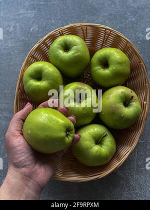 Die Hand hält einen Apfel auf dem Hintergrund eines Korbes Mit Äpfeln Stockfoto