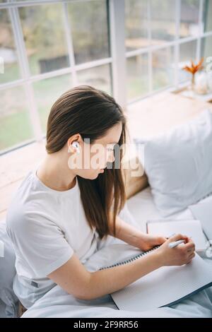 Mädchen schreibt in einem Notizbuch und hört Musik in Bett Stockfoto