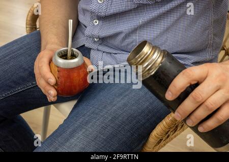 Der sitzende Mann gießt heißes Wasser aus einer Thermoskanne zu Yerba Mate Stockfoto