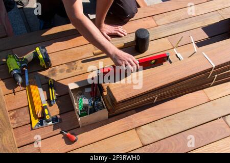 IPE Holz Terrasse Deck Konstruktion, Blick auf Tischlerhand mit Blase Ebene und Holzbearbeitungswerkzeuge während der Installation eines Decks, tropische Hartholz-Terrasse Stockfoto