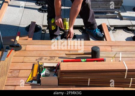 IPE Holz Terrasse Deck Konstruktion, Blick auf Tischlerhände mit einem Schraubendreher und Holzbearbeitungswerkzeuge während der Installation eines Deck, tropisches Hartholz Stockfoto