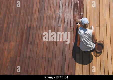 Holzdeck Renovierung Behandlung, die Person, die schützende Holzfleck mit einem Pinsel, Draufsicht der ipe Hartholz-Terrasse Restaurierungsprozess Stockfoto