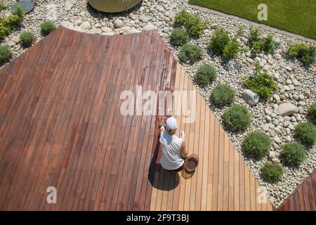 Jährliche Wartung des ipe-Holzdecks im Außenbereich, professioneller Deckarbeiter, der Öl auf gereinigte und geschliffene Ipe-Holzbretter aufgibt Stockfoto