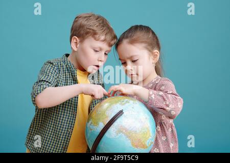 Zwei kleine Kinder untersuchen gemeinsam den großen Globus und stehen gegen den Blauer Hintergrund Stockfoto