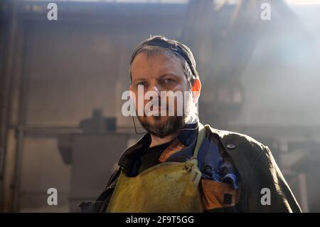 Ein Arbeiter mit einem Bart in Overalls in einem Produktionsraum in einer Fabrik. Nahaufnahme. Stockfoto