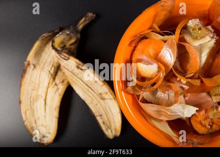 Bananenschalen und andere Schalen aus der Küche in orangefarbenem Teller, auf schwarzem Hintergrund, Nahaufnahme. Stockfoto