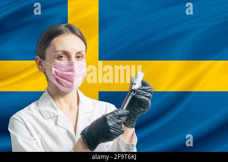 Die Ärztin bereitet die Impfung vor dem Hintergrund der schwedischen Flagge vor. Impfkonzept Schweden. Stockfoto
