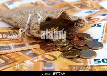 Ein Textilbeutel, gefüllt mit Münzen auf dem Hintergrund der Euro-Banknoten, Nahaufnahme Stockfoto