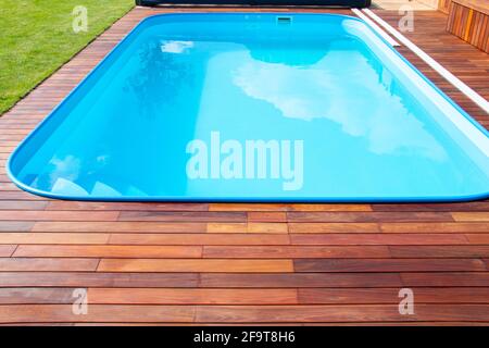 Swimmingpool mit Ipe-Holzterrasse und grünem Gras. Exotisches Hartholz, Ipe-Terrasse neben dem Swimmingpool aus nächster Nähe Stockfoto