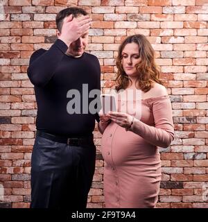 Ein erwachsener Mann und eine Schwangere schauen auf das Telefon. Schwangerschaftsprobleme und Hilfe online Stockfoto