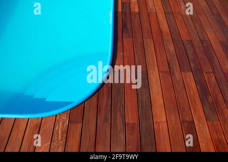 IPE Holzterrasse um den Rand des Swimmingpools. Terrassendesign am Pool, blaues Wasser im Kontrast zu tropischem Hartholz Stockfoto