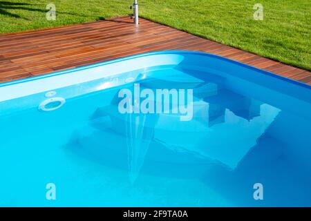 Swimmingpool mit Ipe-Holzterrasse und grünem Gras. Exotisches Hartholz, Ipe-Terrasse neben dem Swimmingpool aus nächster Nähe Stockfoto