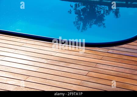 IPE Holzterrasse und Swimmingpool aus nächster Nähe. Gartenterrasse am Pool, blaues Wasser im Kontrast zu tropischen Hartholzplatten. Stockfoto