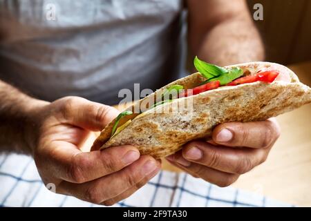 Piadina Romagnola mit Mozzarella-Käse, Tomaten, Schinken und Rucola in den Händen eines Mannes. Italienisches Fladenbrot oder offenes Sandwich. Selektiver Fokus. Stockfoto