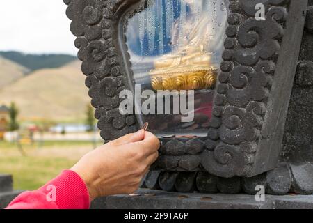 Ein Besucher platziert eine Münze in der Nähe einer umschlossenen goldenen Buddha-Statue, um Glück zu haben, im Garten der tausend Buddhas in Arlee, Montana, USA Stockfoto