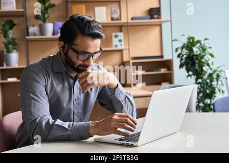 Seriöser indischer Geschäftsmann, der Videoanruf mit verschiedenen Menschen auf dem Laptop hat. Stockfoto
