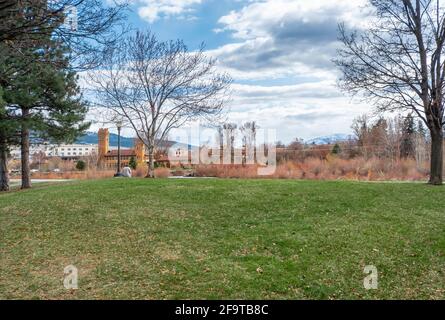 Eine Frau entspannt sich in einem öffentlichen Park entlang des Clark Fork River mit der Innenstadt von Missoula, Montana, USA, in der Ferne. Stockfoto