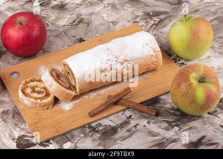 Apfelrolle oder Strudel auf einem Schneidebrett, Zimtstangen und frische Äpfel. Hausgemachte Apfelrolle. Stockfoto