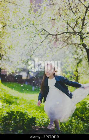 Kleines Mädchen in schwarzer Jacke und weißem Kleid tanzen in Der Kirschgarten im Frühling Stockfoto