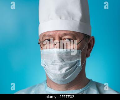 Porträt eines erfahrenen Arztes mittleren Alters in medizinischer Kleidung und einer Maske, die eine Brille trägt. Nahaufnahme der Kamera Stockfoto